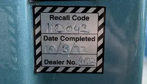 Recall sticker between the vehicle driver's door hinges